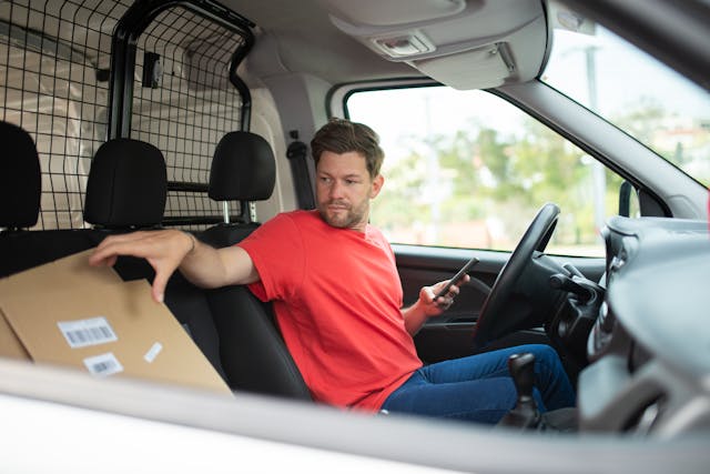 a-man-sitting-in-the-driver-sear-of-a-van-holding-a-cardboard-box